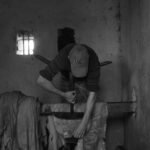 Black and white photo of an artisan hammering leather by hand